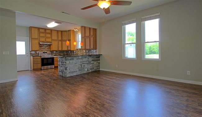 Kitchen with stainless steel range with electric cooktop, brown cabinetry, visible vents, and dark wood-style floors | Image 5