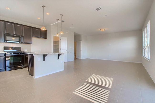 Kitchen featuring black appliances, open floor plan, a breakfast bar area, light tile patterned floors, and light stone counters | Image 11