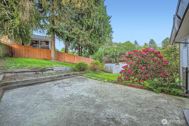 Large open patio off kitchen sliding glass door. Can see greenhouse and part of shed in background. | Image 31