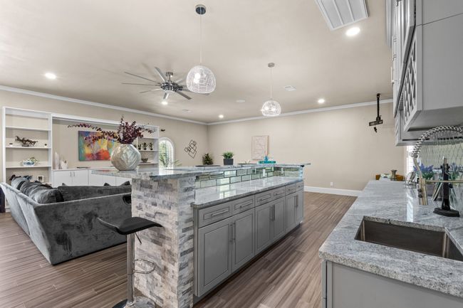 Kitchen featuring gray cabinets, wood finished floors, ceiling fan, ornamental molding, and light stone counters | Image 25