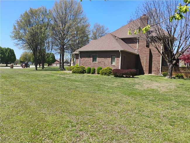 View of property exterior featuring brick siding, a yard, roof with shingles, and a chimney | Image 5