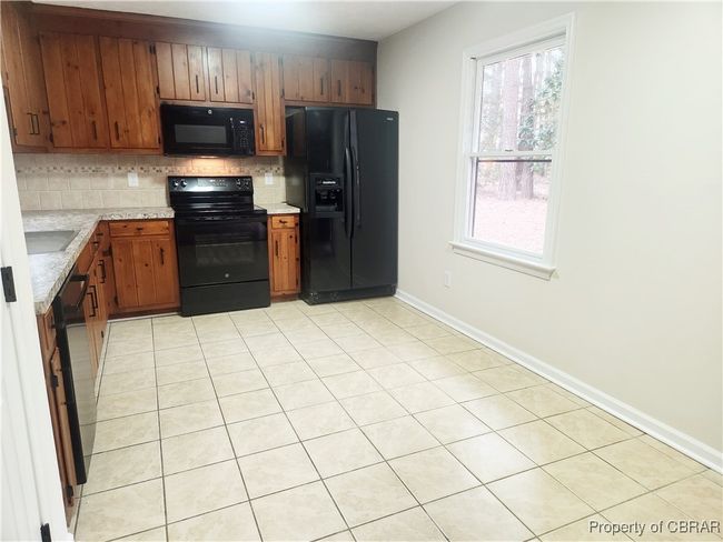 Kitchen featuring a healthy amount of sunlight, light tile patterned floors, decorative backsplash, and black appliances | Image 4