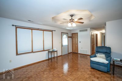 Large living room with parquey wood flooring, trey ceiling with fan, and corner coat closet. Solid wood 6-pane doors through out house. | Image 2