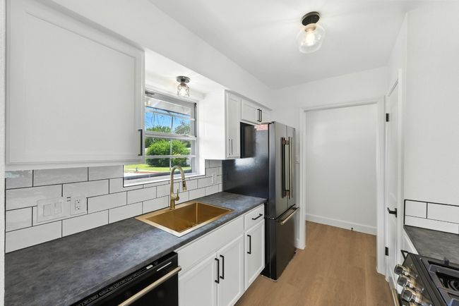 Kitchen with dark countertops, light wood-type flooring, decorative backsplash, and black appliances | Image 11