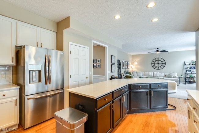 Kitchen with stainless steel refrigerator with ice dispenser, a center island, a textured ceiling, open floor plan, and ceiling fan | Image 7
