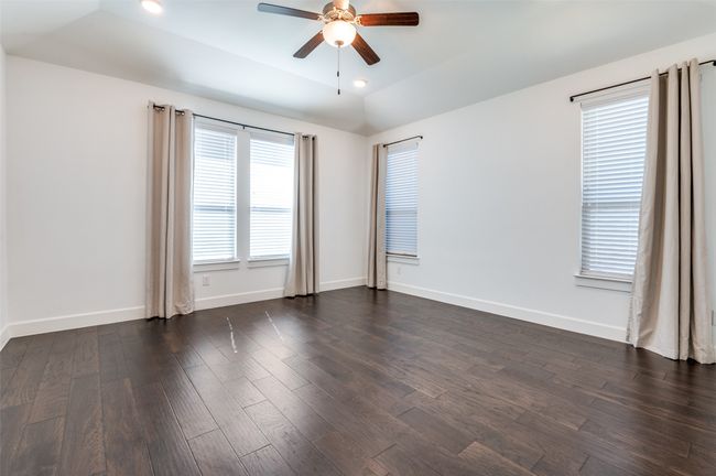Step into the inviting master bedroom, featuring rich dark wood flooring, a sleek ceiling fan, elegant baseboards, and soft recessed lighting for a warm and relaxing ambiance. | Image 14