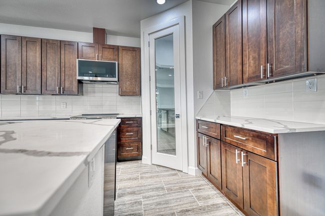 Kitchen with dark brown cabinetry, light stone counters, and light wood-type flooring | Image 29