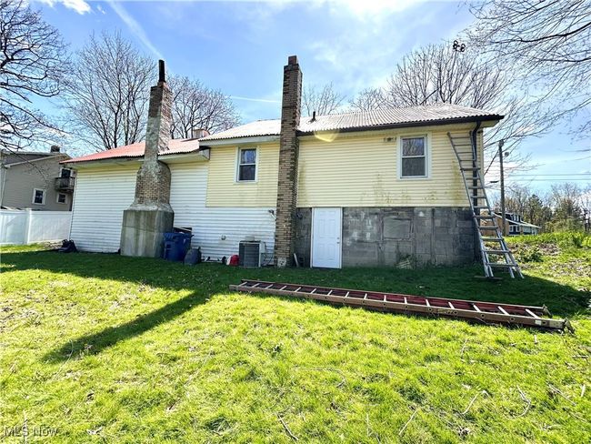 Rear view of house with a chimney, central air condition unit, fence, a yard, and metal roof | Image 24