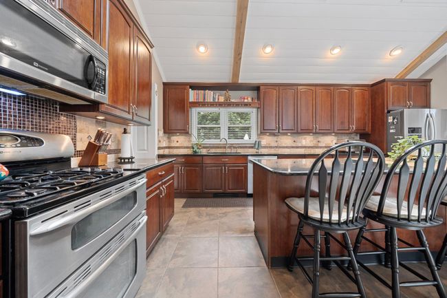 Kitchen with appliances with stainless steel finishes, a breakfast bar, a center island, dark countertops, and backsplash | Image 18