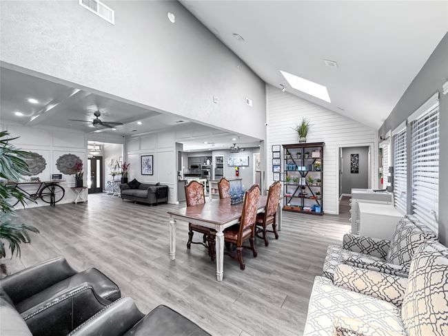 Dining space with light wood finished floors, high vaulted ceiling, a skylight, a ceiling fan, and a decorative wall | Image 10