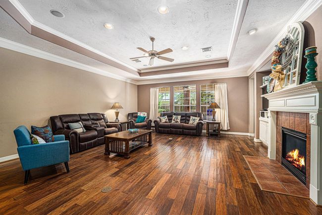 This spectacular living room showcases beautiful flooring, a cozy fireplace, and tray ceilings with crown molding, offering a warm and welcoming atmosphere for everyday living or entertaining. | Image 10