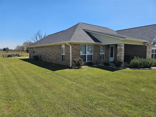 View of side of home with central air condition unit, a shingled roof, and a yard | Image 6