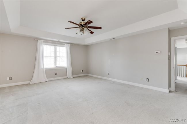 Primary bedroom with a tray ceiling, a ceiling fan, light colored carpet, and a smoke detector | Image 26
