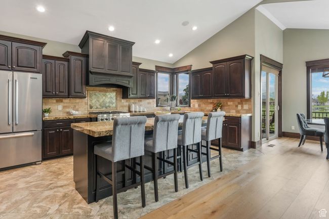 Kitchen with high quality fridge, dark brown cabinetry, backsplash, a kitchen bar, and a kitchen island | Image 4