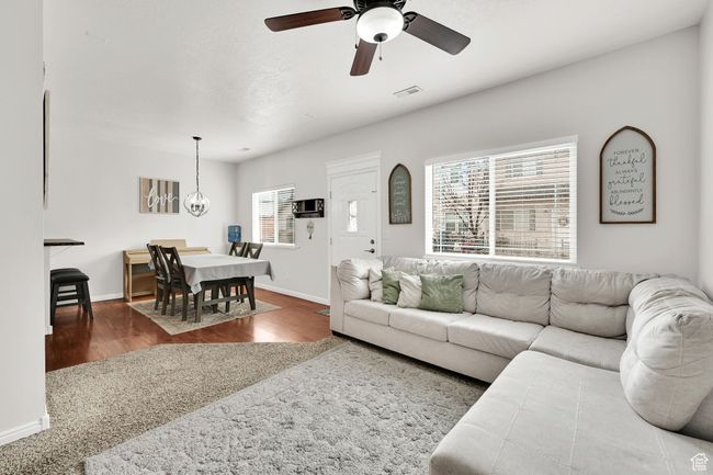 Living room with visible vents, ceiling fan with notable chandelier, baseboards, and wood finished floors | Image 9