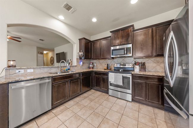 Kitchen with appliances with stainless steel finishes, dark brown cabinets, decorative backsplash, light stone countertops, and a ceiling fan | Image 8