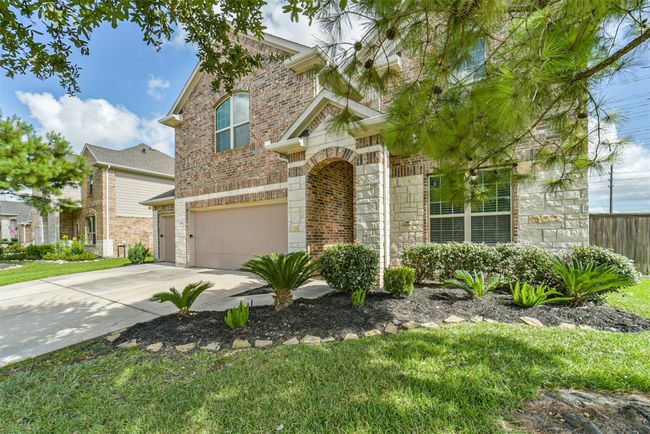 This two-story brick home features a well-maintained front yard with lush greenery and a spacious driveway leading to a two-car garage. The arched entryway adds charm, and mature trees provide shade and privacy. | Image 32