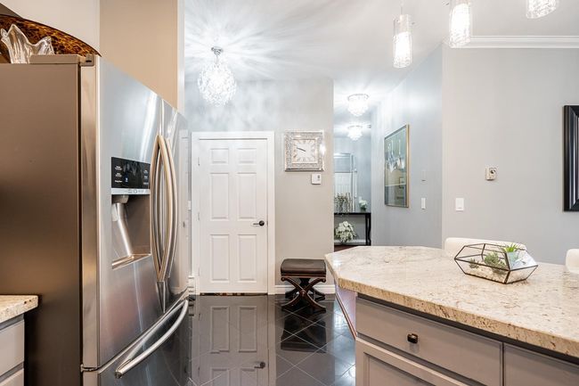 Kitchen with light stone counters, hanging light fixtures, crown molding, dark tile patterned floors, and stainless steel fridge | Image 7