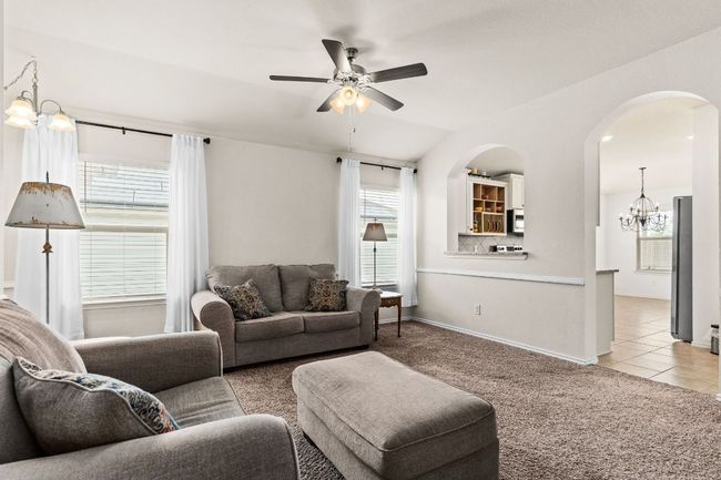 Living room featuring light tile patterned floors, baseboards, arched walkways, ceiling fan with notable chandelier, and light colored carpet | Image 7