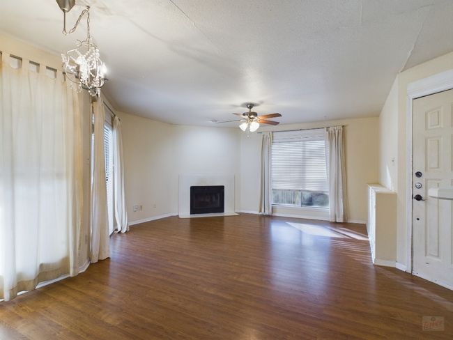 Unfurnished living room featuring baseboards, dark wood-style flooring, a fireplace with flush hearth, and ceiling fan with notable chandelier | Image 4