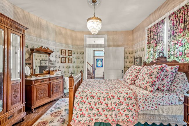 Bedroom with wallpapered walls, wood finished floors, and a notable chandelier | Image 22