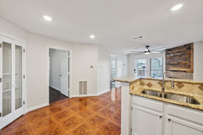 Kitchen featuring a dual sink, recessed lighting, white cabinetry, ceiling fan, and tasteful tumble marble backsplash. Opens to living and dining areas. | Image 9
