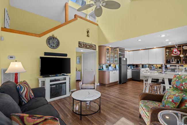 Living area featuring dark wood-type flooring, a high ceiling, ceiling fan, and a glass covered fireplace | Image 12