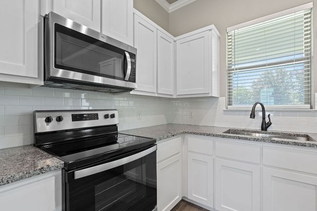 Kitchen featuring appliances with stainless steel finishes, ornamental molding, white cabinets, decorative backsplash, and light stone countertops | Image 14