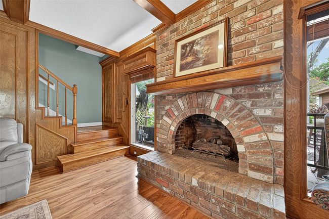 The brick fireplace commands attention with antique-inspired charm, framed by dual picture windows. Nearby, a wide staircase adds architectural interest and connects the vintage warmth of the space to the upper level. | Image 17