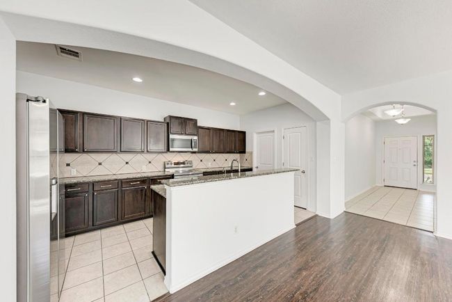 Kitchen featuring stainless steel appliances, dark brown cabinetry, tasteful backsplash, light stone countertops, and a center island with sink | Image 17