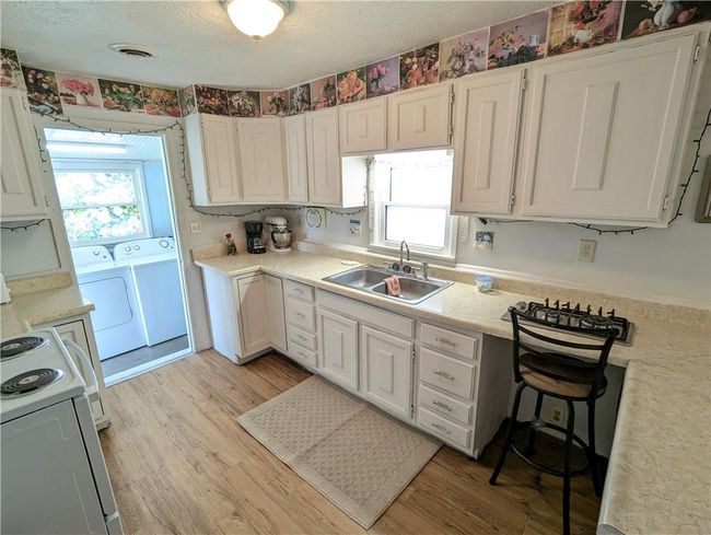 Kitchen with light wood-style floors, washer and clothes dryer, light countertops, and a sink | Image 19