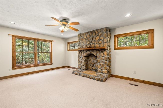 Living room featuring a textured ceiling, a wealth of natural light, ceiling fan, and a stone fireplace | Image 31