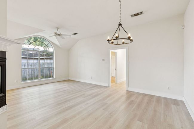 Unfurnished living room featuring ceiling fan, light wood-style floors, a chandelier, lofted ceiling, and a glass covered fireplace | Image 12