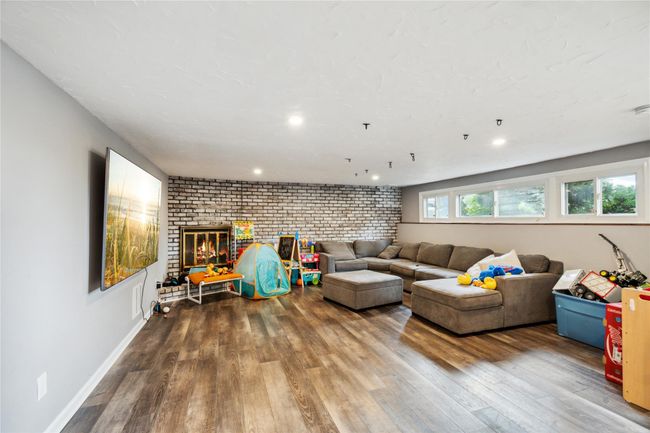 Living room with brick wall, wood finished floors, a fireplace, and recessed lighting | Image 16