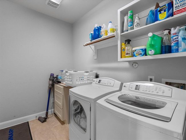 This photo features a bright laundry room with a washer and dryer, ample shelving for storage, and a compact utility area, making it convenient for household tasks. | Image 38