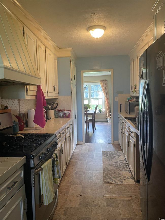Kitchen with freestanding refrigerator, stainless steel gas range oven, custom exhaust hood, tasteful backsplash, and tile counters | Image 9