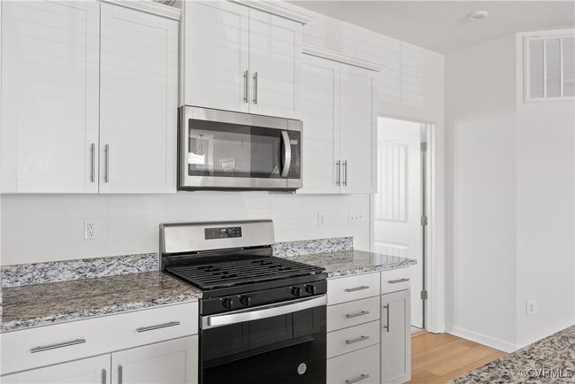 Kitchen featuring appliances with stainless steel finishes, light stone counters, light wood finished floors, baseboards, and visible vents | Image 14