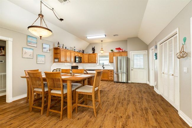 This inviting kitchen features warm wooden cabinetry, stainless steel finish appliances, and a spacious dining area with a modern light fixture. The open layout and vaulted ceiling enhance the airy feel, ideal for gatherings. | Image 8