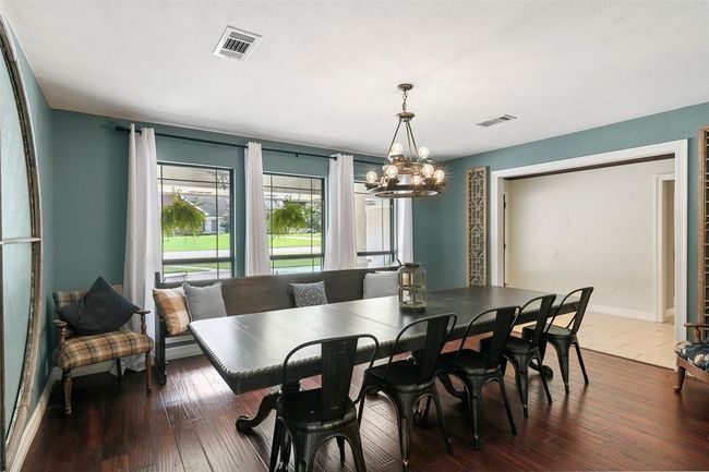 This spacious dining room features a large table with seating for eight, hardwood floors, and ample natural light from three windows. The room is accented with a modern chandelier and has a cozy, inviting atmosphere. | Image 14