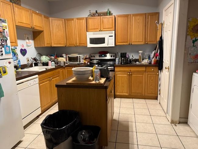 Kitchen featuring white appliances, light tile patterned floors, a kitchen island, dark countertops, and a sink | Image 4