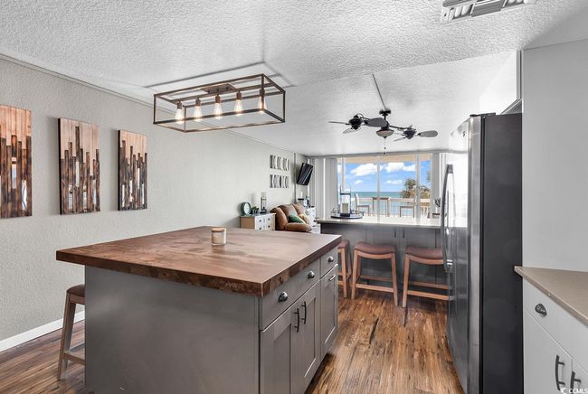 Kitchen featuring dark wood-style flooring, a breakfast bar, wood counters, ceiling fan, and freestanding refrigerator | Image 19