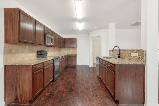 Kitchen featuring stainless steel appliances, a sink, dark wood finished floors, light stone countertops, and decorative backsplash | Image 14