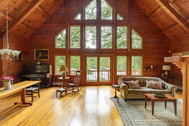 Living room with high vaulted ceiling, wood ceiling with exposed beams, light wood-style floors, wood walls, and a chandelier | Image 9