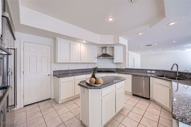Kitchen with dishwasher, wall chimney exhaust hood, dark stone countertops, a sink, and light tile patterned flooring | Image 29