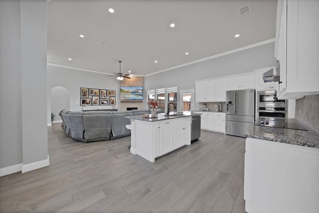 Kitchen featuring appliances with stainless steel finishes, a sink, a tiled fireplace, a ceiling fan, and arched walkways | Image 13