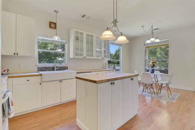 Kitchen with butcherblock island, farmhouse sink, light wood finished floors, stove, and hanging light fixtures | Image 8