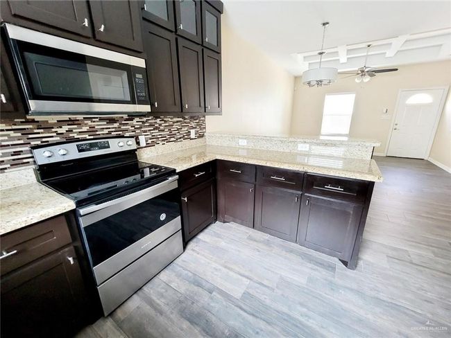 Kitchen with stainless steel appliances, a peninsula, tasteful backsplash, light wood-style flooring, and beam ceiling | Image 7