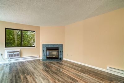 Unfurnished living room featuring a baseboard radiator, a tiled fireplace, a textured ceiling, and hardwood / wood-style floors | Image 2