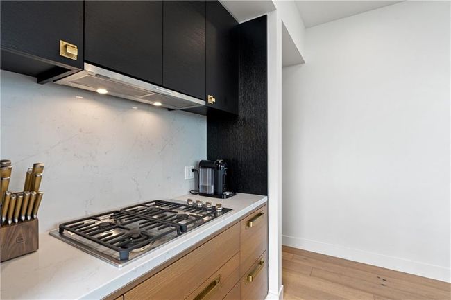 Kitchen with extractor fan, stainless steel gas stovetop, light wood-style floors, dark cabinets, and backsplash | Image 10