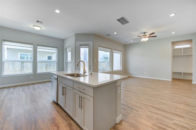 This open-concept living space features a modern kitchen with a central island and sink, adjacent to a bright dining area with large windows. | Image 13